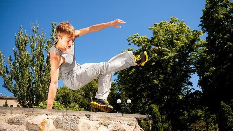 Young man in sportswear practicing parkour outside on stone wall on clear summer day Young man in sportswear practicing parkour outside on stone wall on clear summer day with blue sky at background. Active lifestyle and extreme sports concept
